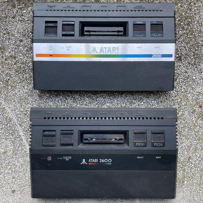 Due modelli di Atari 2600jr affiancati e fotografati dall'alto. Un Atari 2600jr classico con frontalino in acciaio ed un Atari 2600 Black Irish, completamente nero.